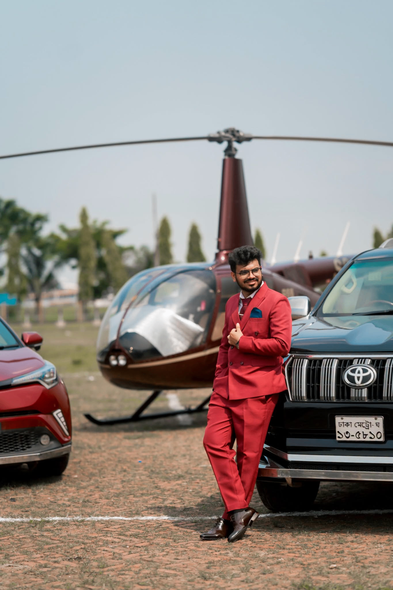 Portrait of Nerob Pikash in a red suit standing beside a vehicle